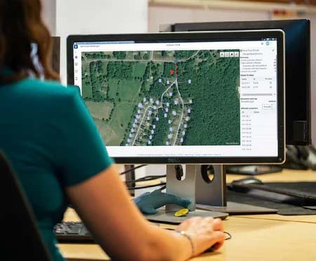 A person sits at a desk looking at a computer monitor displaying a satellite map with marked locations, using MicroStation to plan new campuses. | Bentley Systems | Infrastructure Engineering Software Company A person sits at a desk looking at a computer monitor displaying a satellite map with marked locations, using MicroStation to plan new campuses.